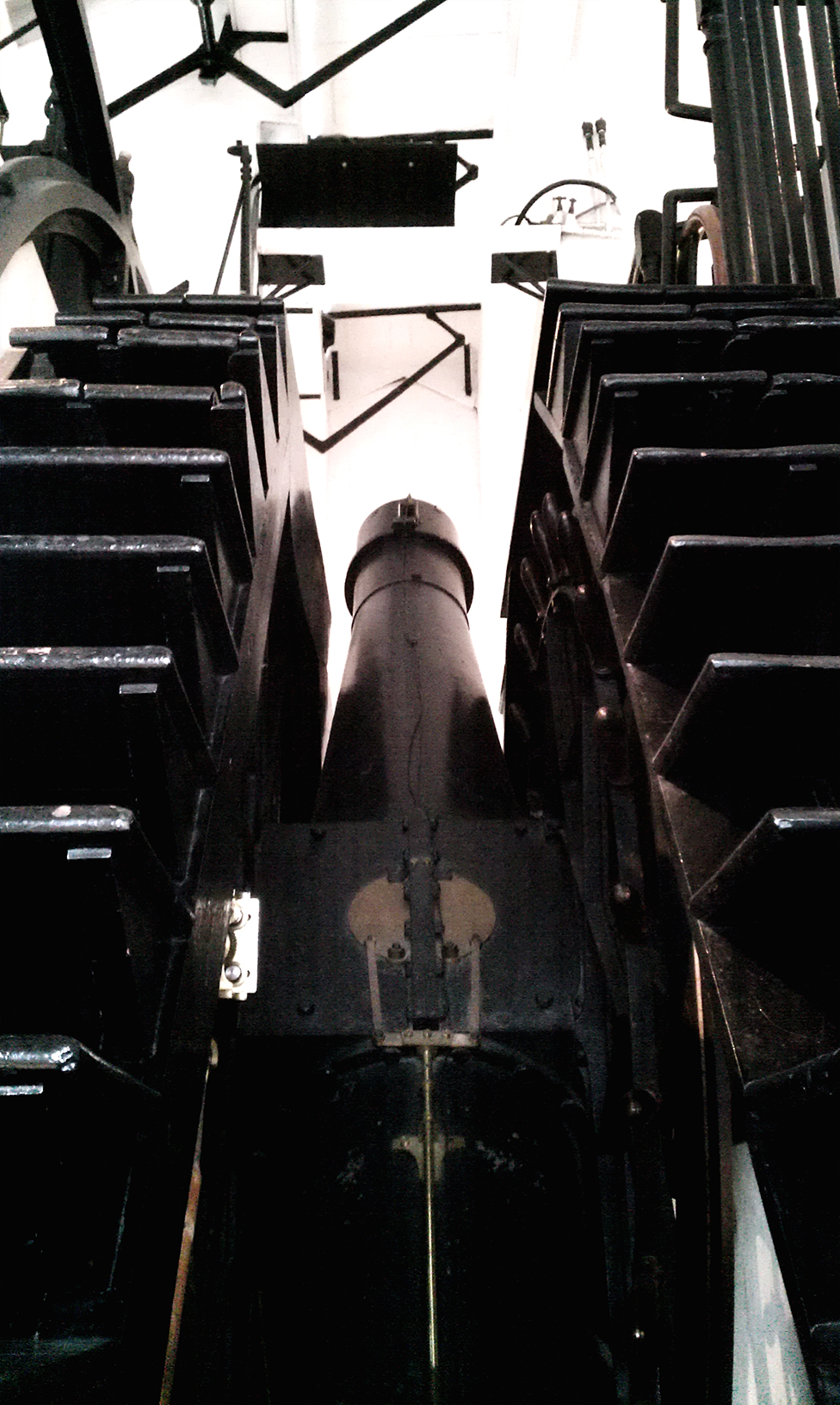 A nineteenth-century telescope mounted on stone piers inside a observatory room, its barrel pointing through a slit in the wall toward the sky.