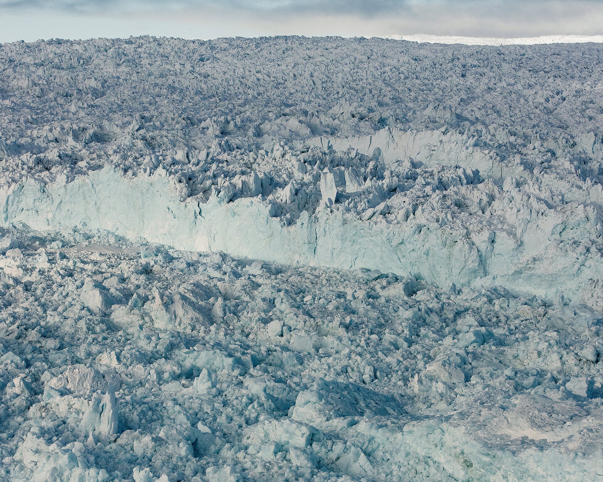 A vast Antarctic or Greenland ice sheet seen from the air, white with visible crevasse fields flowing toward the sea.