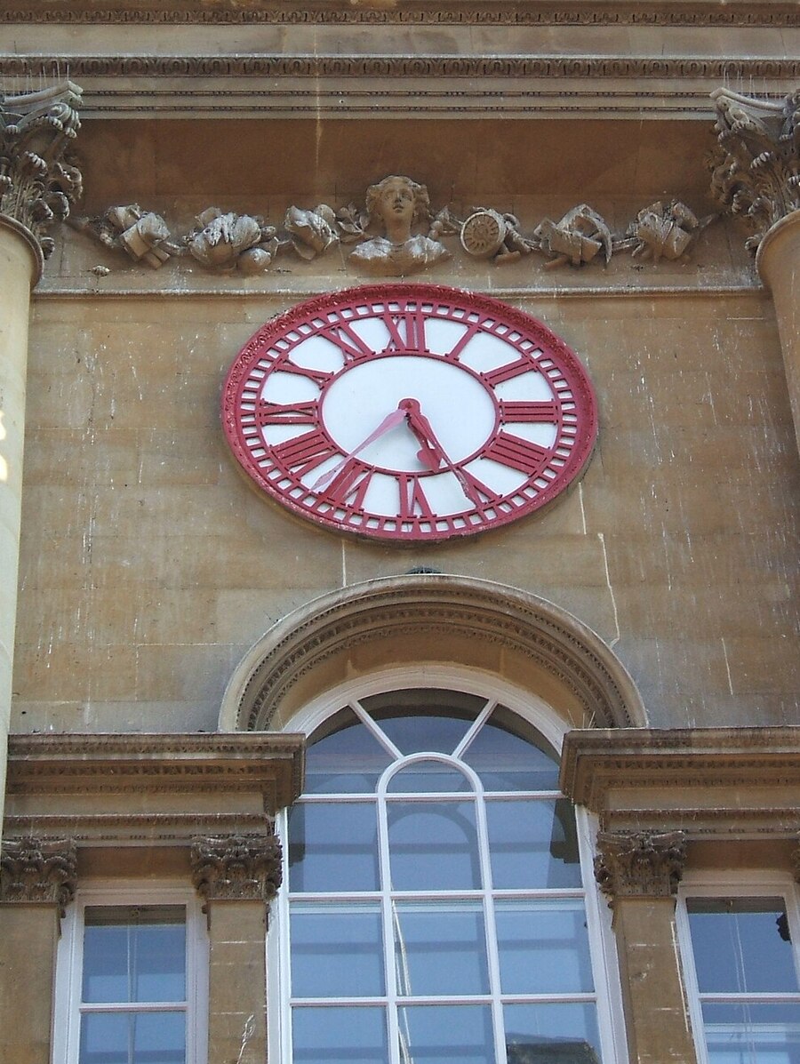 The clock on the Corn Exchange in Bristol, its red iron dial carrying two minute hands offset from one another.