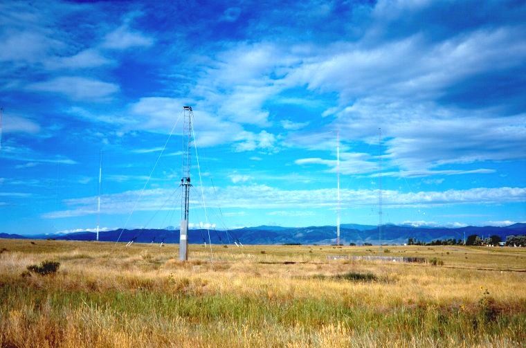 Shortwave antenna towers and masts at a radio station site, standing in open grassland under a wide sky.